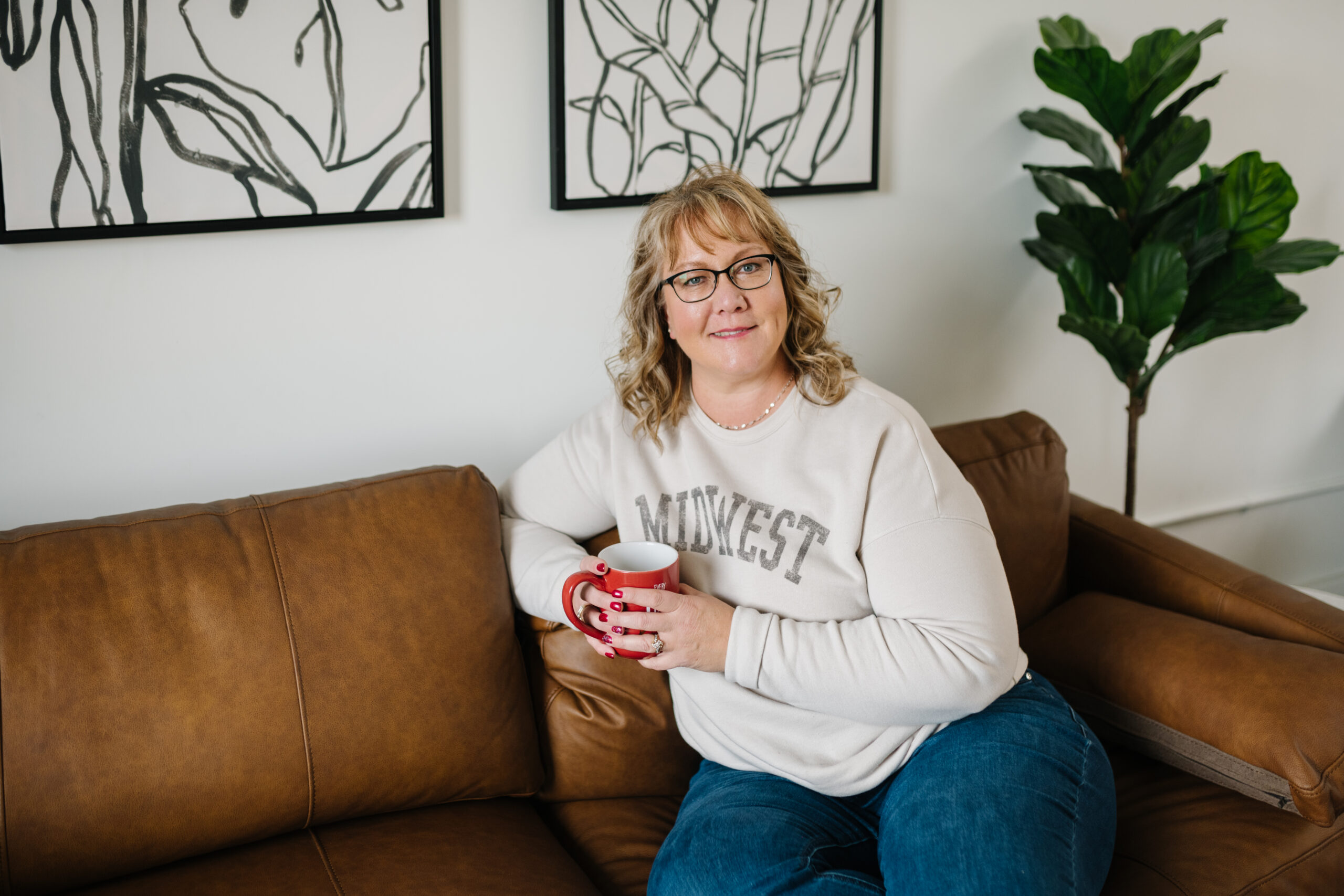 Sara Ricke sitting with a cup of coffee on a tan sofa